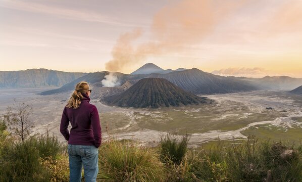 Tourist in front of landscape at sunset, smoking volcano Gunung Bromo, Mt. Batok at front, Mt. Kursi at back, Mt. Gunung Semeru, Bromo Tengger Semeru National Park, Java, Indonesia