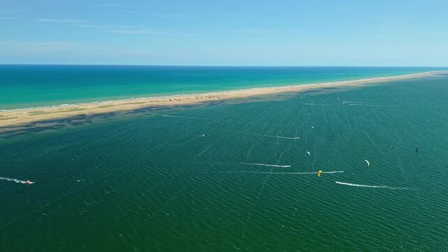 Aerial view of kitesurfers and colorful kites near Punta del Fangar sandbar in Ebro Delta, Spain. Drone panorama of shallow lagoon, turquoise Mediterranean waters 
