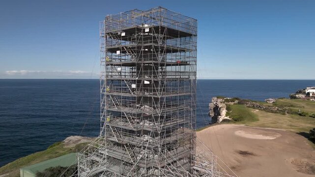 Old sewage tower in Bondi built in the early twentieth century under restoration from aerial view. Camera orbits structure in CW direction revealing Pacific Ocean, beach, and surrounding urban area.