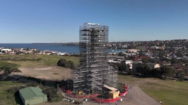 Old sewage tower in Bondi built in the early twentieth century under restoration from wide aerial view. Camera orbits structure in CCW direction revealing Pacific Ocean, beach and urban area.