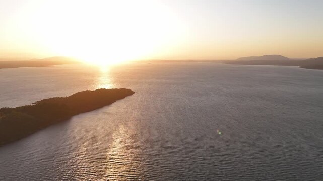 Aerial view of wooded peninsula at golden hour, calm lake, distant Andes.