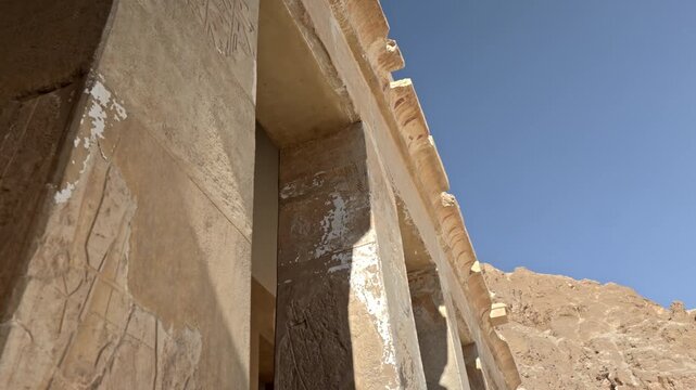 A low-angle close-up looking up at a corner section of the stone architecture at Queen Hatshepsut's Mortuary Temple (Deir el-Bahari) in Luxor, Egypt.