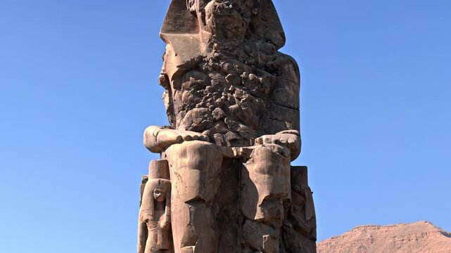 A medium, low-angle shot focusing entirely on the weathered upper half of one of the Colossi of Memnon in Luxor, Egypt.