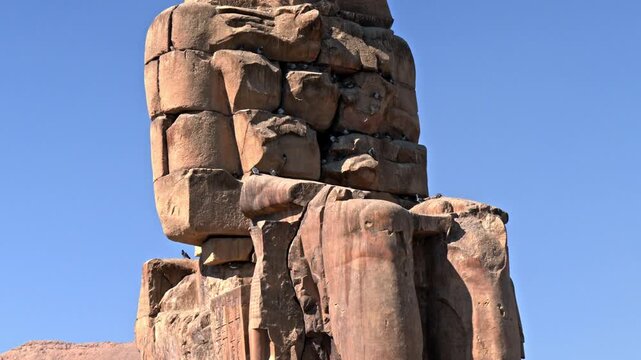 A medium, low-angle shot showing the upper portion of the second Colossus of Memnon on the West Bank of Luxor, Egypt.