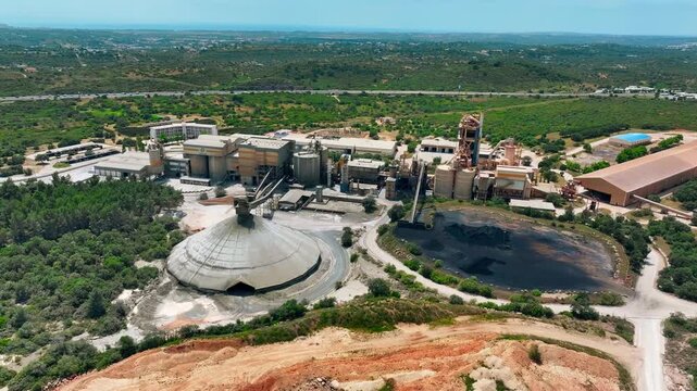 Aerial view of cement production facility showing limestone quarry operations and aggregate processing. Heavy machinery and conveyor systems transport materials across the site.