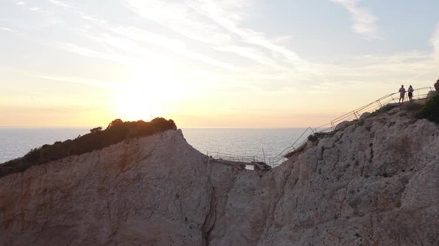 Drone footage flying forward toward a glowing sunset above the iconic white cliffs of Porto Katsiki in Lefkada, Greece. Golden evening light, dramatic coastal scenery and the tranquil Ionian Sea creat