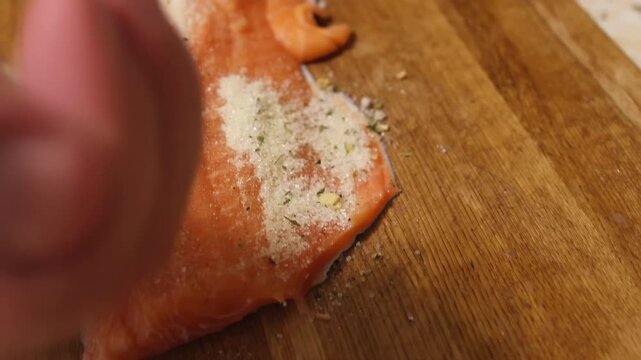 Person rubbing spices onto raw salmon on chopping board. Culinary preparation of seafood before cooking, highlighting healthy eating, homemade meals in modern kitchen environment.