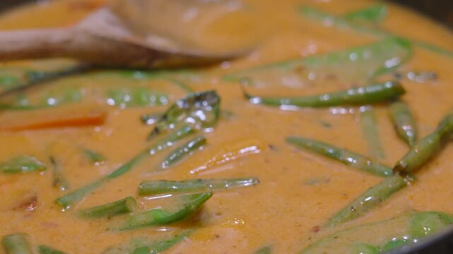 Side View of Delicious, Fresh Vegetable Thai Red Curry Simmering in Hot Pan with Green Beans, Mangetout, Carrots, Baby Sweetcorn. Classic Asian Food.