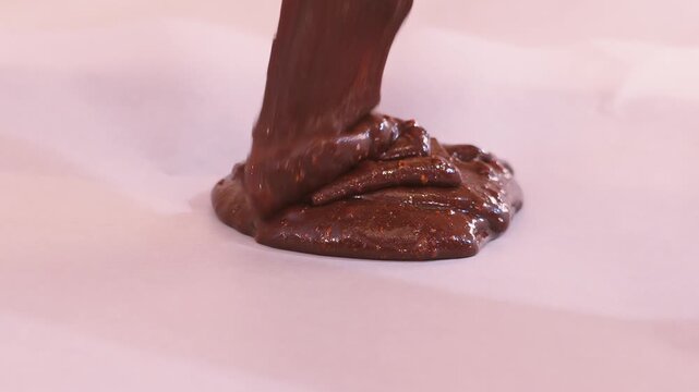 Pouring Thick Chocolate Brownie Batter Onto Greaseproof Paper in Baking Sheet. Thick fudge batter ribbons and folds onto itself as it drops. Satisfying food texture. 4K.
