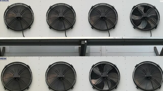 Industrial HVAC condenser fans spinning on refrigeration unit outdoors