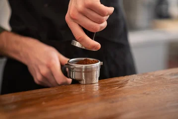 A close up of a barista pressing ground coffee with a metal tamper into a portafilter © Nomad_Soul