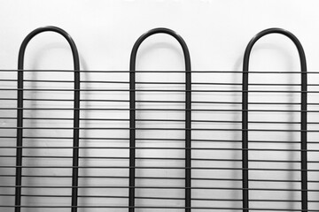 Black metal refrigerator condenser coils forming a horizontal and vertical grid pattern on a white wall © reddish