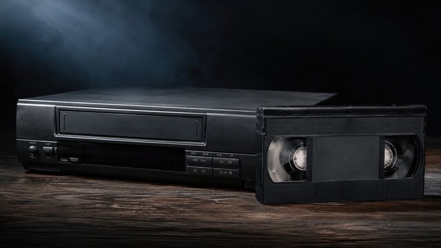 Black VCR player with a VHS video cassette on a wooden surface, shot in moody studio lighting evoking retro analog nostalgia