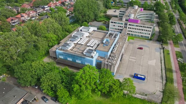 Aerial retreat small data center in Dutch urban area, surrounded by green spaces, houses and parking