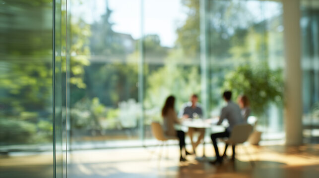 Blurred background of business people working at a table inside a bright modern glass office with a view of green trees