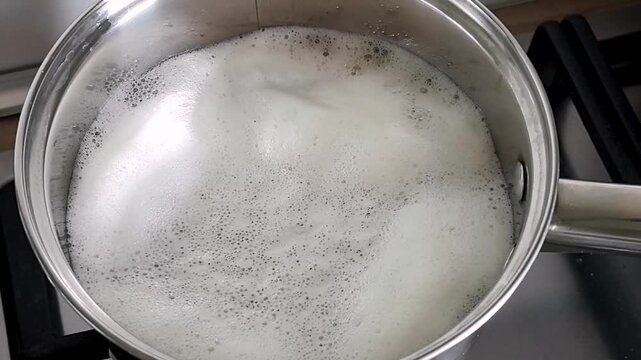 Boiling water with foam bubbles in stainless steel pot on gas stove