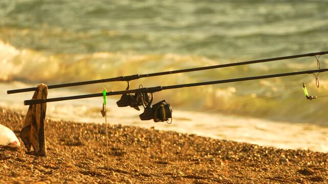 Fishing sea sunset, rods fixed on a pebble beach waiting for a catch during golden hour near ocean waves