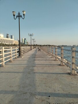 Long waterfront pier with street lamps extending toward the sea under a clear sky.