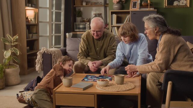 Long shot of senior Caucasian grandparents playing board game with young grandsons in living room. Clip showcases multigenerational family bonding, perfect for retirement planning or toy commercials