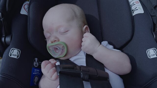 Newborn baby boy sleeping in a car seat and gently sucking on a pacifier