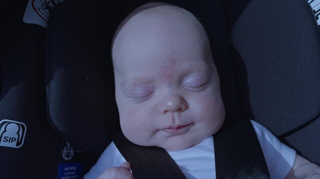 Newborn baby boy crying and thrashing in a car seat with arms and legs flailing, in slow motion.