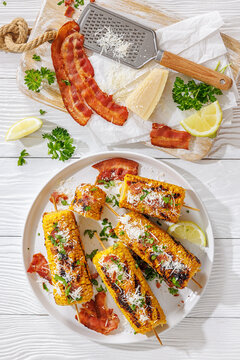 Maize cobs on skewers are served with bacon