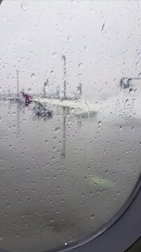 Passenger view through aircraft window as ground crew performs aircraft deicing procedure during snowfall and freezing winter conditions before departure.