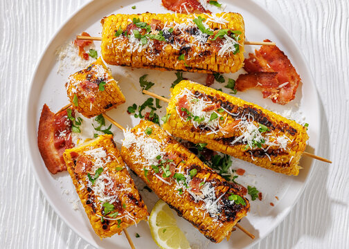 Maize cobs on skewers are served with bacon