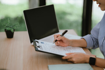 Fototapeta premium HR professional reviewing a resume on a clipboard beside a laptop, evaluating candidate qualifications during a recruitment and hiring process.