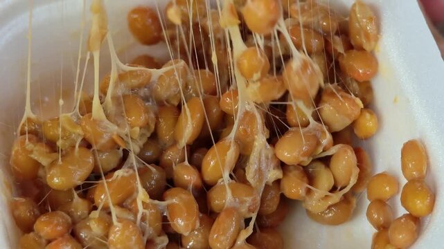 Chopsticks lifting sticky fermented natto soybeans.