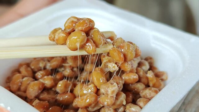 Chopsticks lifting sticky fermented natto soybeans.