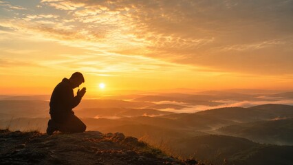 Fototapeta premium Silhouette of a kneeling person praying at sunrise on a mountain ridge, overlooking misty, layered valleys