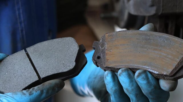 A car mechanic shows two car brake pads, an old one and a new one, close-up.