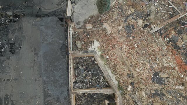 An aerial close-up view reveals the charred metal and wooden skeletal frame of a building devastated by fire. The structure shows severe damage with burnt beams, ash, and collapsed roofing components.