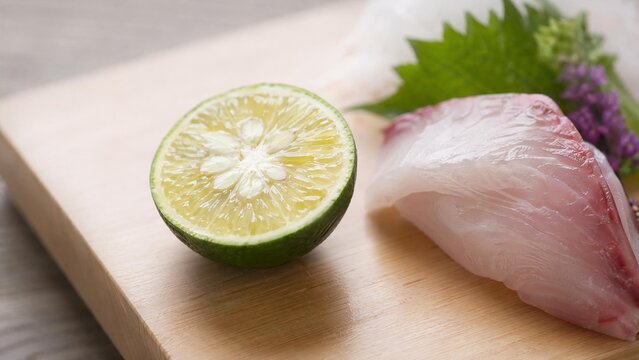 A halved sudachi fruit on a Japanese cutting board next to a piece of sashimi.
