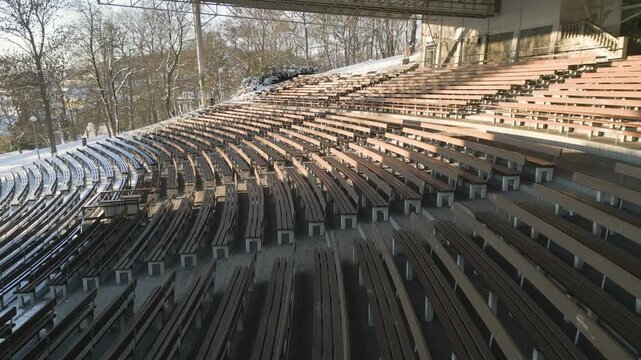 An elevated drone winter view of the open-air summer cinema in &Uacute;st&iacute; nad Labem shows rows of empty, snow-covered amphitheater seating and a large projection screen under a massive metal roof structure 