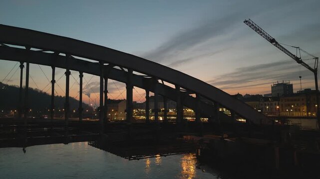 Aerial drone night twilight view of &Uacute;st&iacute; nad Labem of arched Dr. Edvard Bene&scaron; Bene&scaron;ův most Bridge stretching across the Labe River. The background captures glowing city lights, railway station sunset