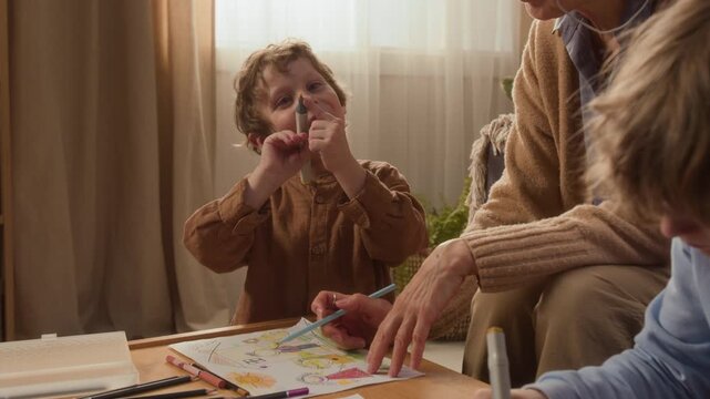 Handheld shot of senior grandmother teaching young children how to draw with colorful markers at home. Footage is ideal for family bonding campaigns or early childhood education promotions
