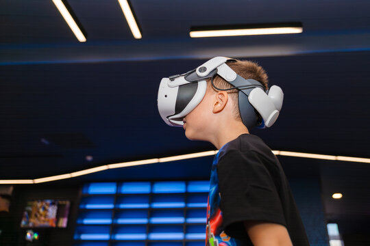 Boy wearing VR glasses stands in a futuristic space with blue lights while exploring virtual reality games and experiences indoors