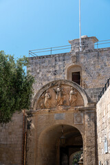 Obraz premium view from behind mdina gate, malta with limestone brick and detailed statues above the archway with clear blue skies overhead in summer sunlight and green lush tree to the left