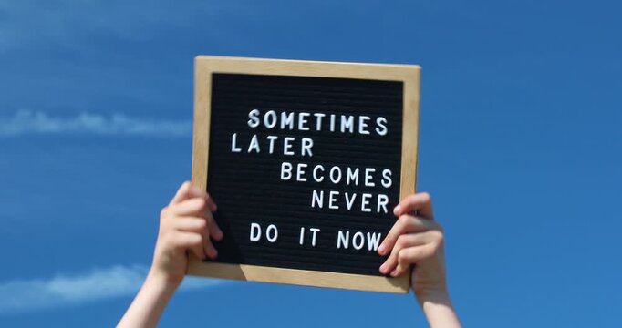 Young female hands holding a letter board with Inspirational motivational quote Sometimes later becomes never. Do it now words against blue sky outdoors