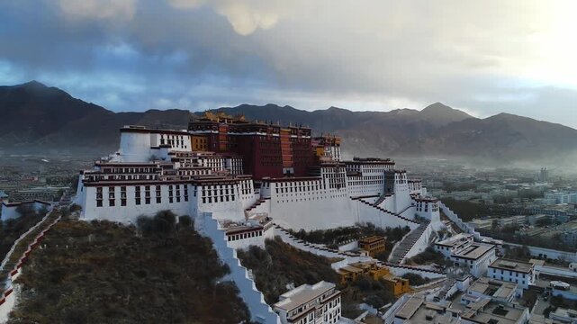 Aerial view of the Potala Palace at sunrise in Lhasa, Tibet, China, with the historic palace on the hill overlooking the city, surrounded by mountains and morning mist under golden light.