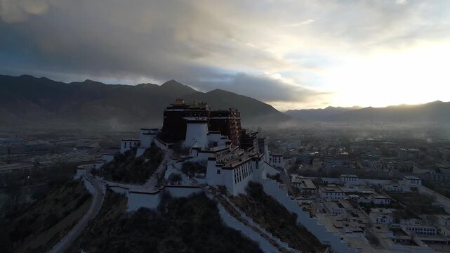 Aerial view of the Potala Palace at sunrise in Lhasa, Tibet, China, with the historic palace on the hill overlooking the city, surrounded by mountains and morning mist under golden light.