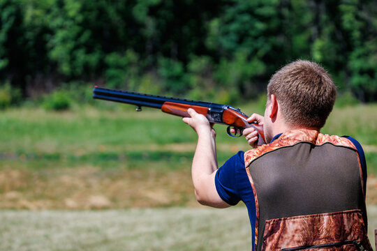 Young man aiming a double-barreled shotgun at a clay target shooting range, outdoor skeet and trap shooting sport