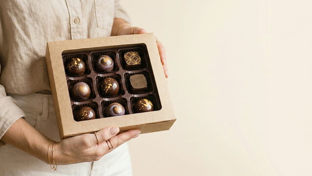 Chocolates: Person holding artisan chocolate gift box with gourmet truffles against minimalist background, for luxury dessert and celebration concept.