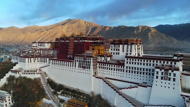 Aerial view of the Potala Palace at sunrise in Lhasa, Tibet, China, with the historic palace on the hill overlooking the city, surrounded by mountains and morning mist under golden light.
