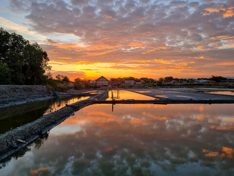 Colorful Sunset Reflections Over Traditional Salt Ponds with Dramatic Cloudy Evening Sky