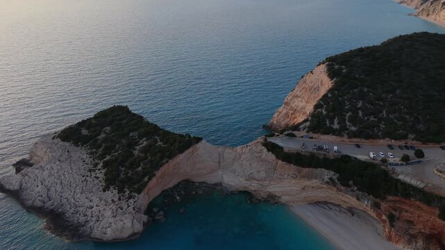 Aerial drone footage descending toward the iconic Porto Katsiki Beach in Lefkada, Greece. Spectacular white limestone cliffs, turquoise Ionian Sea waters, and golden sunset light create a breathtaking