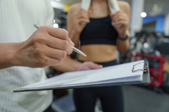 Personal trainer discussing workout plan with client on clipboard in modern gym for fitness coaching