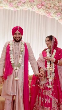 Vertical Shot of Sikh Bride and Groom Holding Hands Up After Varmala Ceremony with Elegant Stage Decor